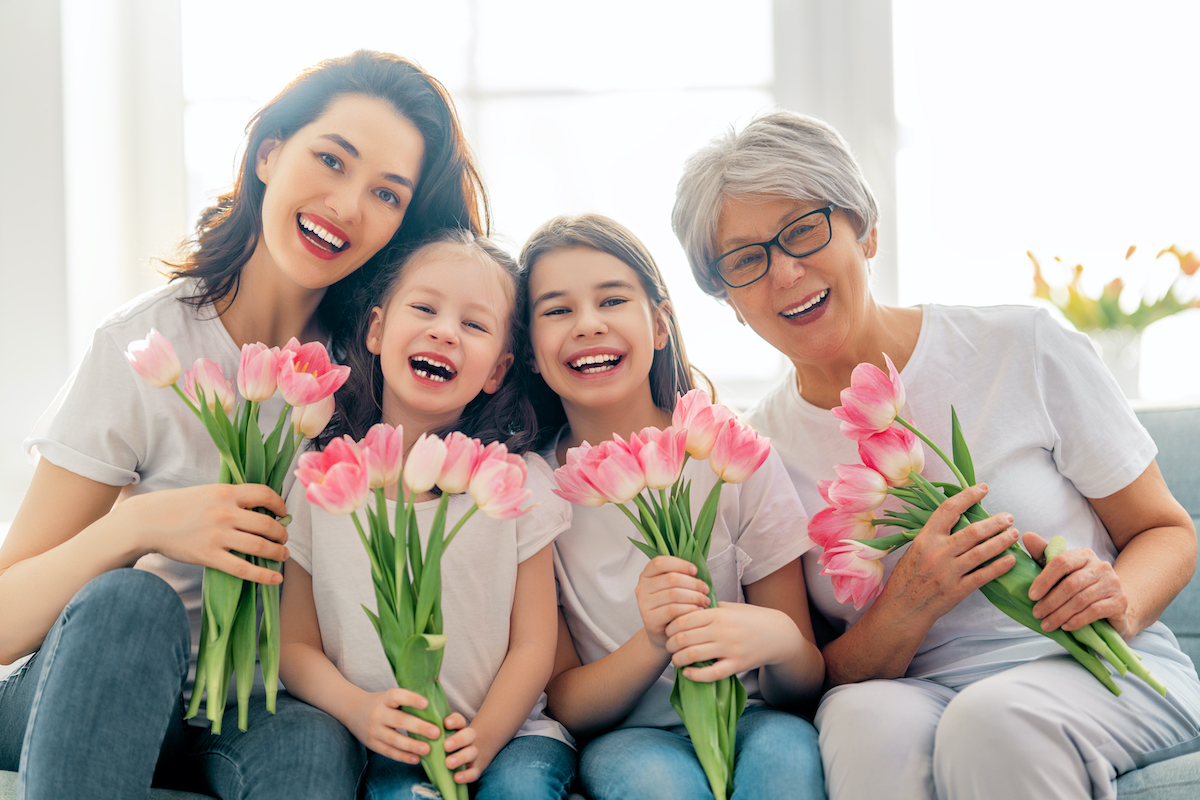Three generations of women hold pink tulips and smile