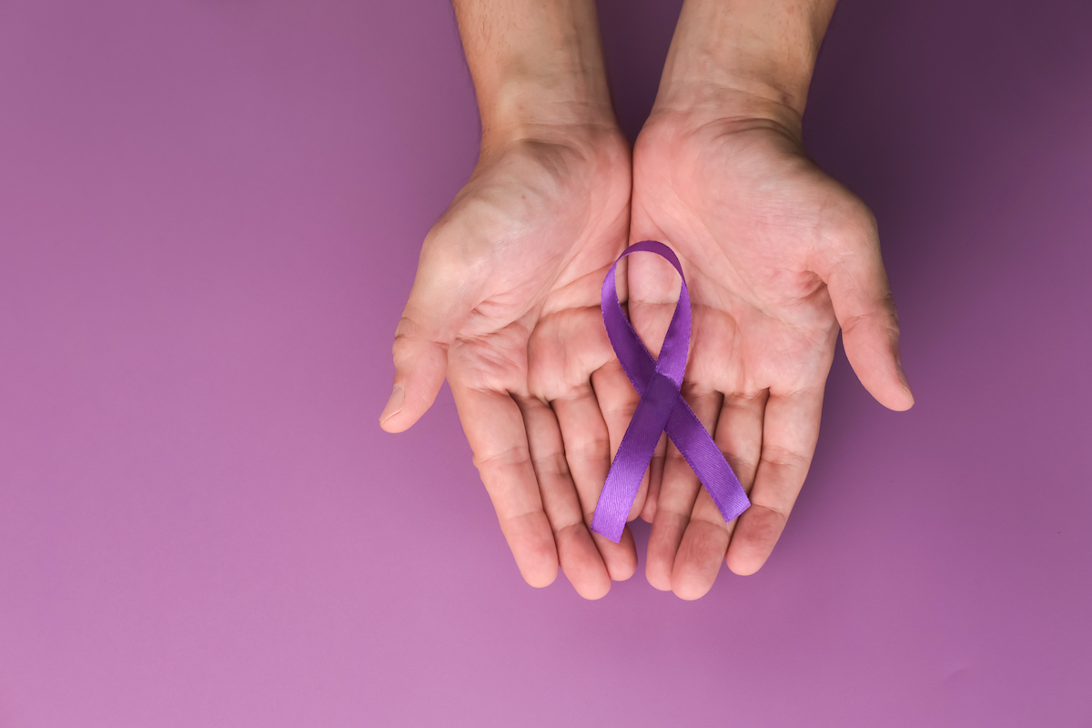 hands hold a purple ribbon in front of a purple background