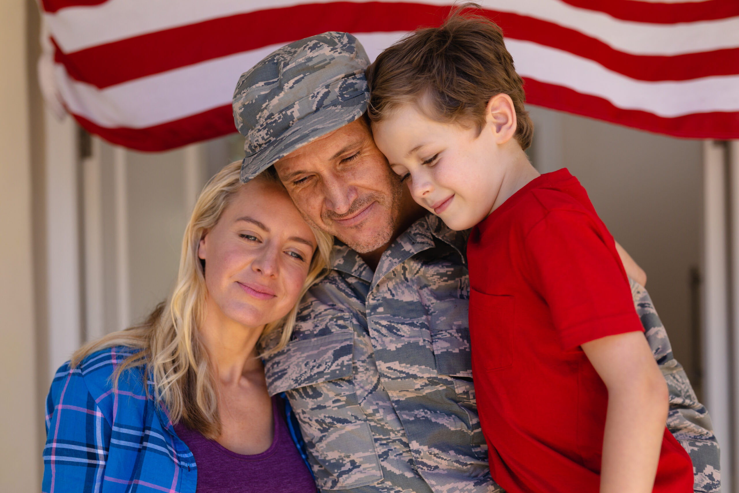 A soldier embraces his family in front of the American Flag on Armed Forces Day